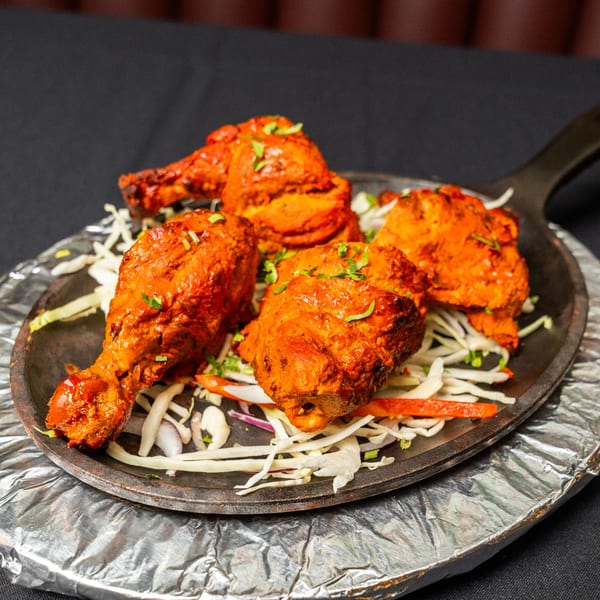 Four pieces of Tandoori chicken, garnished with herbs, served on a bed of shredded cabbage and onions.