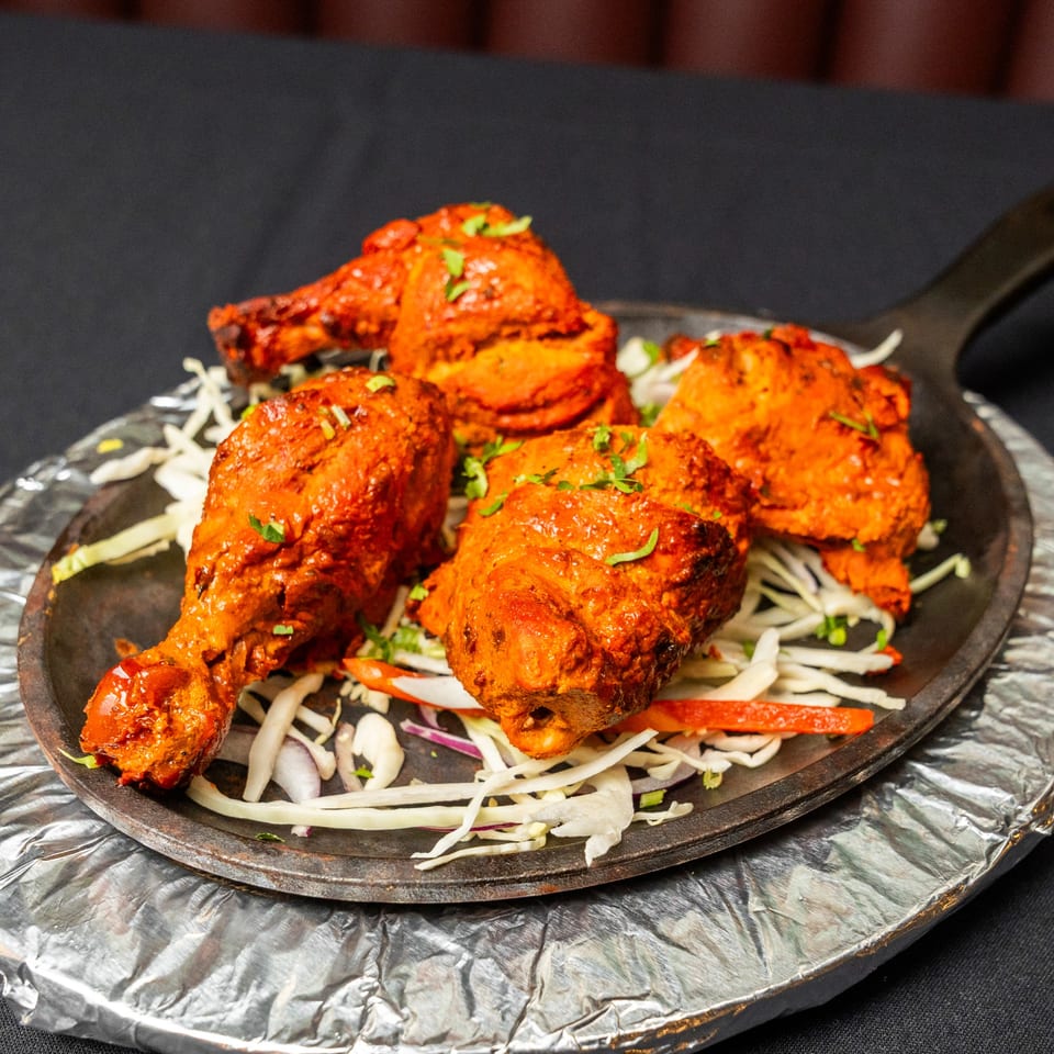 Four pieces of Tandoori chicken, garnished with herbs, served on a bed of shredded cabbage and onions.