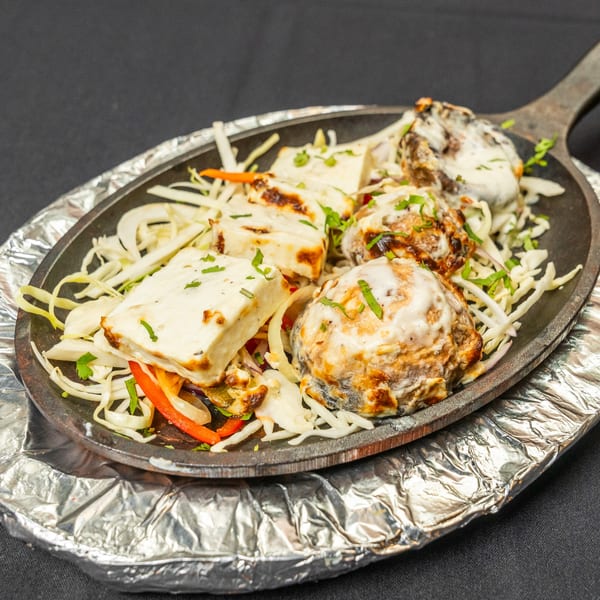 Sizzling platter of paneer and mushroom tikka, garnished with shredded cabbage and peppers.