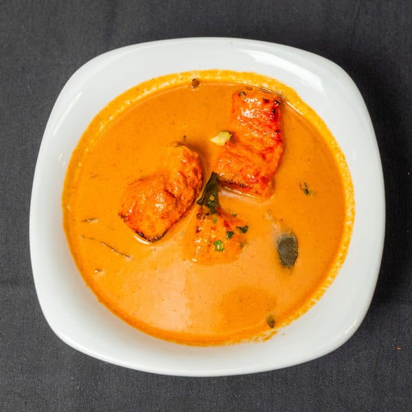 A white bowl filled with orange curry, featuring pieces of chicken and green herbs.