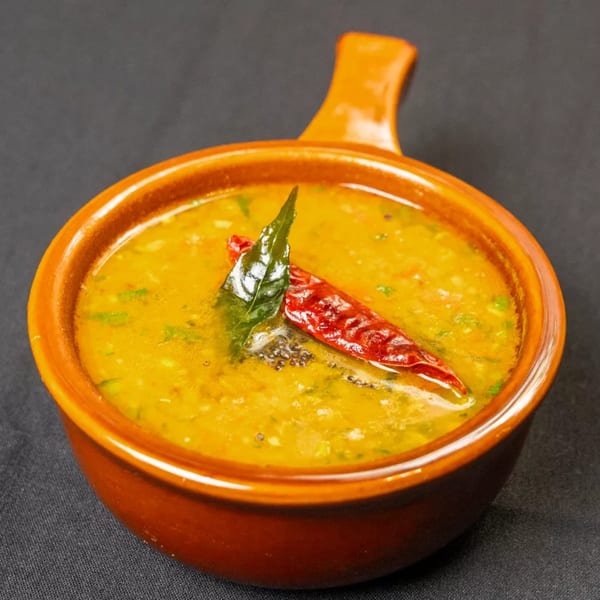 Yellow lentil dal in an orange bowl, garnished with a red chili and curry leaves.