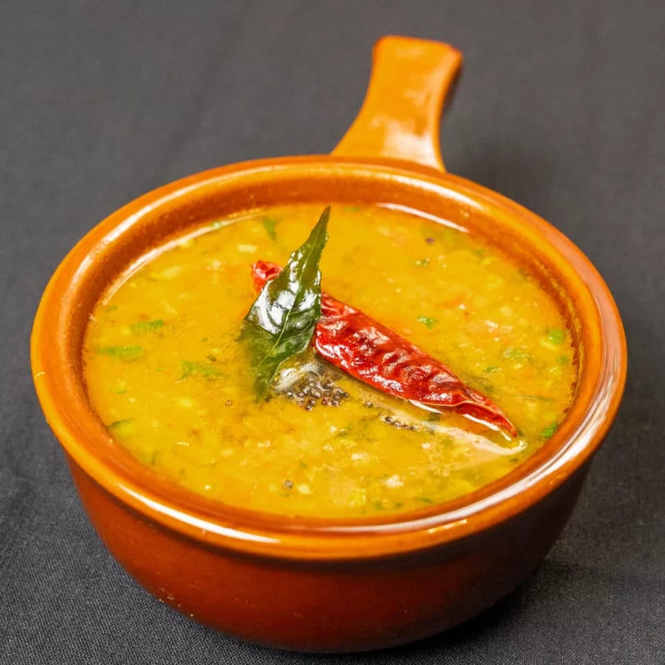 Yellow lentil dal in an orange bowl, garnished with a red chili and curry leaves.