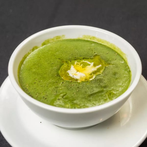 Vibrant green soup with a swirl of cream and a sprinkle of pepper in a white bowl.