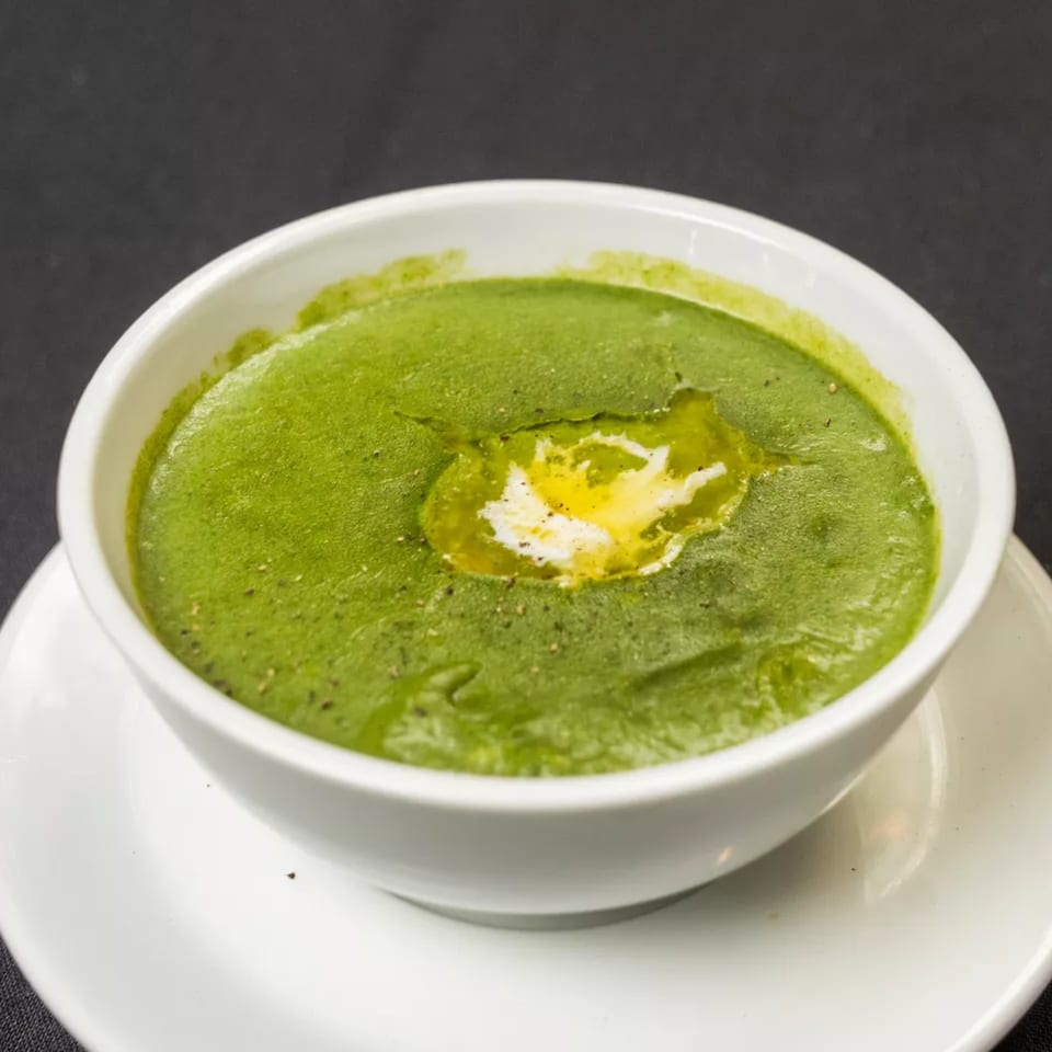 Vibrant green soup with a swirl of cream and a sprinkle of pepper in a white bowl.
