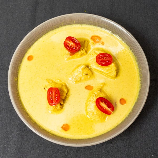 Yellow curry with chicken pieces and halved cherry tomatoes in a gray bowl on a dark surface.