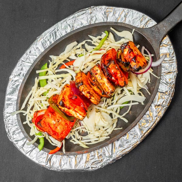 Grilled paneer tikka skewers with bell peppers and onions on a bed of shredded cabbage.