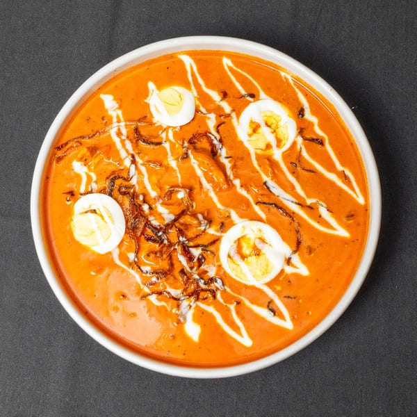 A vibrant orange curry with four halved hard-boiled eggs, drizzled with white cream and crispy fried onions.