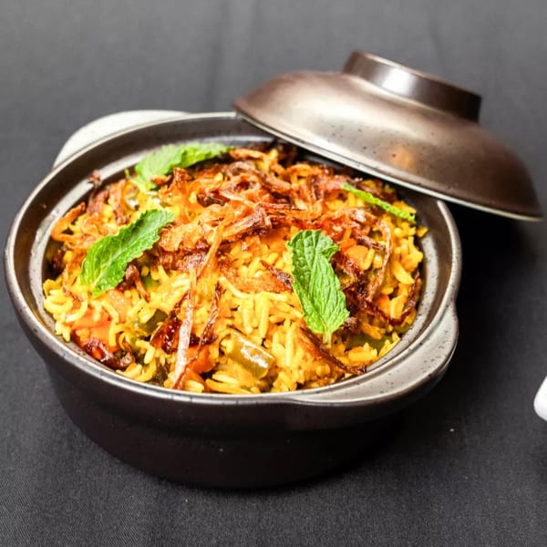 Biryani, a rice dish with fried onions and mint, in a dark pot with a lid.