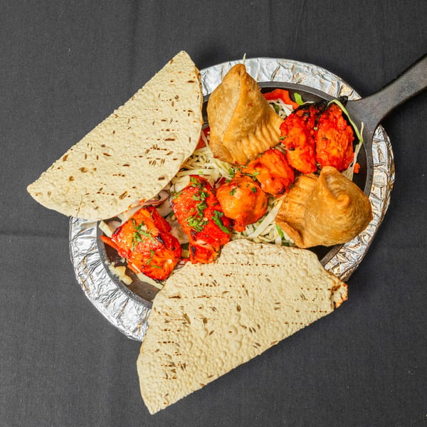 Indian appetizer platter with chicken tikka, samosas, and papadum on a black background.